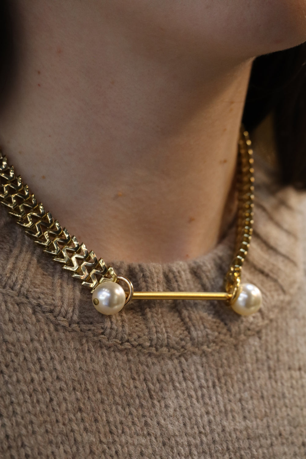 A close-up of a person wearing the Zubeldia Gold Bar and Double Pearl choker, styled over a beige knitted sweater.