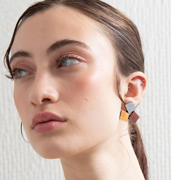 A close-up of a woman wearing a geometric three square stud earring. 