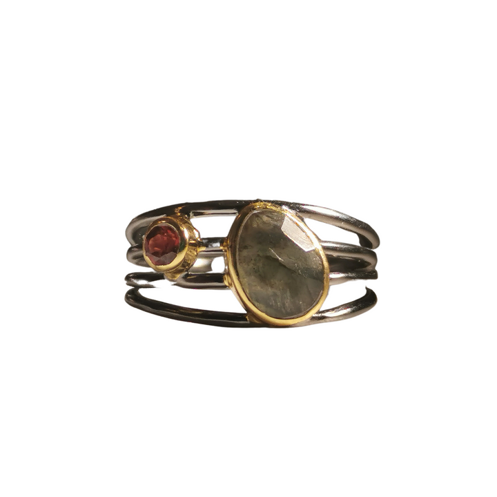 A Watermelon tropical Black Rhodium and Gold Plated Ring with Labradorite and Garnet features two gemstones: a larger, oval-shaped green stone set in a gold bezel, and a smaller, round red stone set in a gold bezel. This piece of handmade jewellery boasts glossy bands and bezels for added elegance.