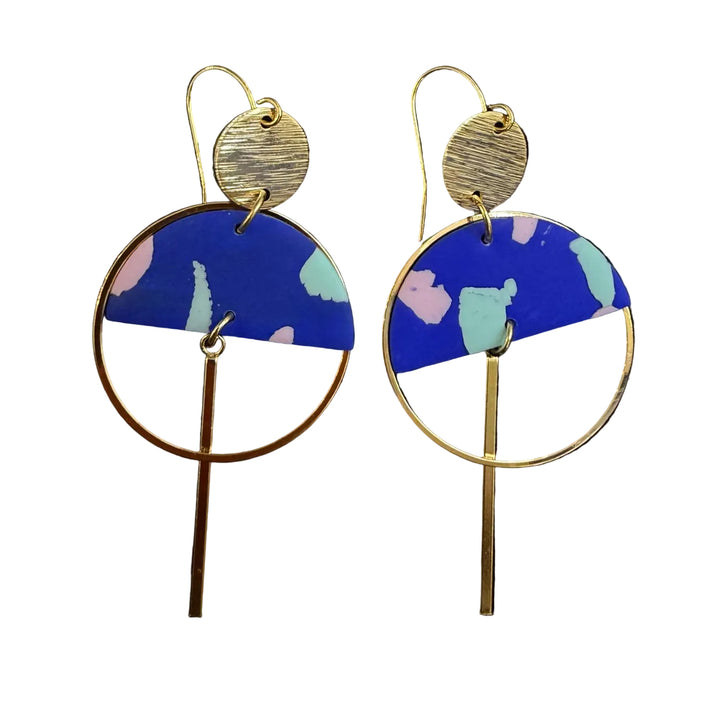 The Sinead Earrings by Kybalion Jewellery feature gold-tone circles and bars, plus blue semicircles with pink, green, and light blue abstract patterns, shown on a black background.