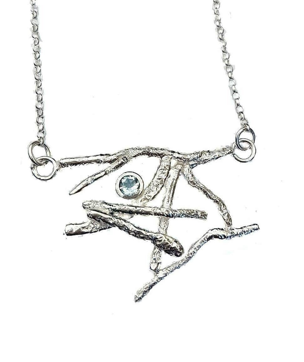 A sterling silver Blue Topaz Faerie Realm Pendant by Caroline Stokesberry-lee, resembling intertwined branches, boasts a small Blue Topaz Gem at its heart. Suspended from an 18inch sterling silver belcher chain against a plain white background, this necklace evokes enchanting elegance.