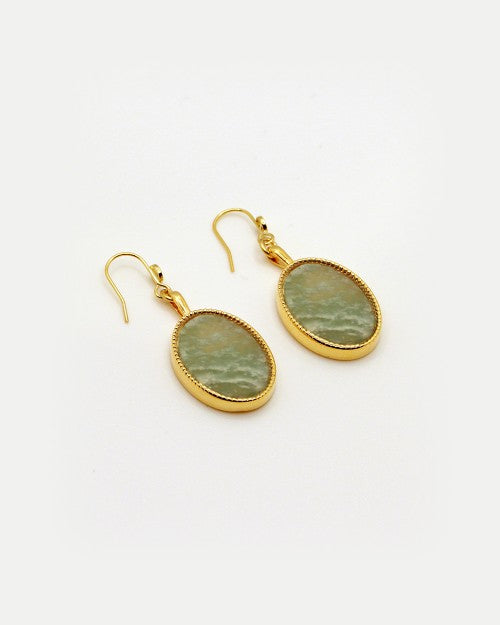 A pair of Frida Earrings in semi-precious green gemstones, finished in 24K gold with an oval-shaped center stone. Handmade by Nilai in Paris, these dangly earrings feature hook-style backs for wearing and are displayed on a plain white background.