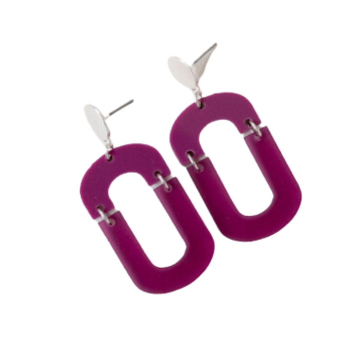 A pair of Studio Nok Nok Magenta Oval Misty Acrylic Silver Earrings featuring large, hollow, oval-shaped magenta pieces made from recycled acrylic, linked to small silver loops at the top. The handmade magenta pieces have smooth edges and are suspended from silver oval posts.