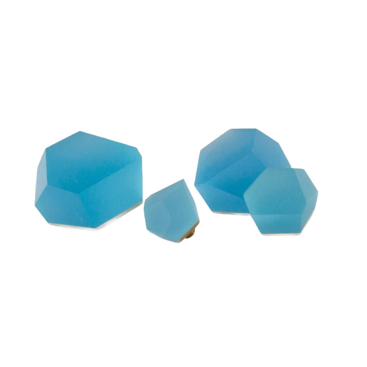 Four blue geometric-shaped objects of varying sizes, arranged on a white background. The shapes, reminiscent of gemstones or crystals, include a hexagon and pentagon. Each piece is crafted from polished acrylic resin with a slightly frosted appearance, creating an elegant display. These are the Fruit Bijoux Ring Top VU Crystals Capri Blue by Fruit Bijoux.