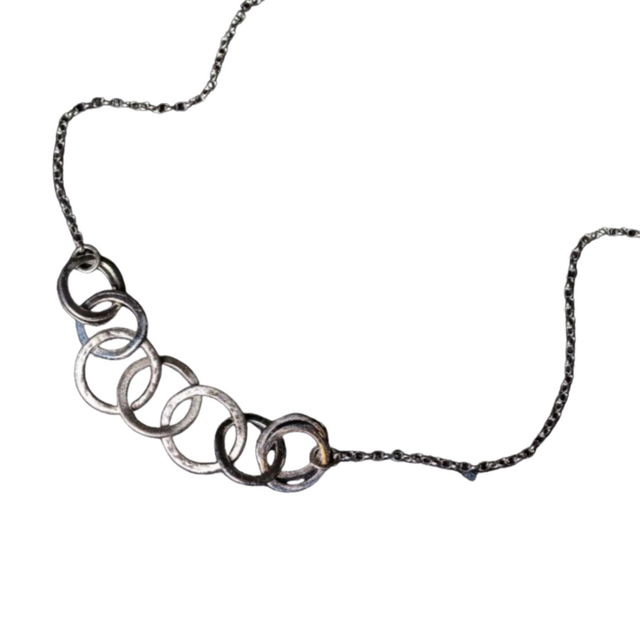 A delicate Carran Chain Necklace by Lynsey de Burca featuring a chain interwoven through a series of linked hollow circles, crafted from a metallic material. The circles are arranged in a horizontal line and gradually change in size. The textured chain has a twisted texture.