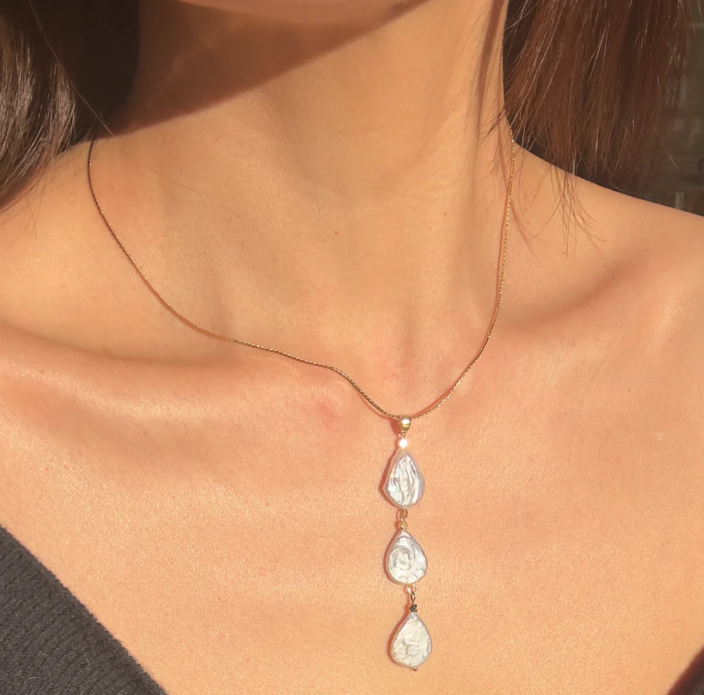 A close-up of a woman's neck wearing the Aria V Cascade Necklace: a gold-plated chain with three handmade, irregular silver pendants crafted in Dublin. Soft lighting highlights this unique design.