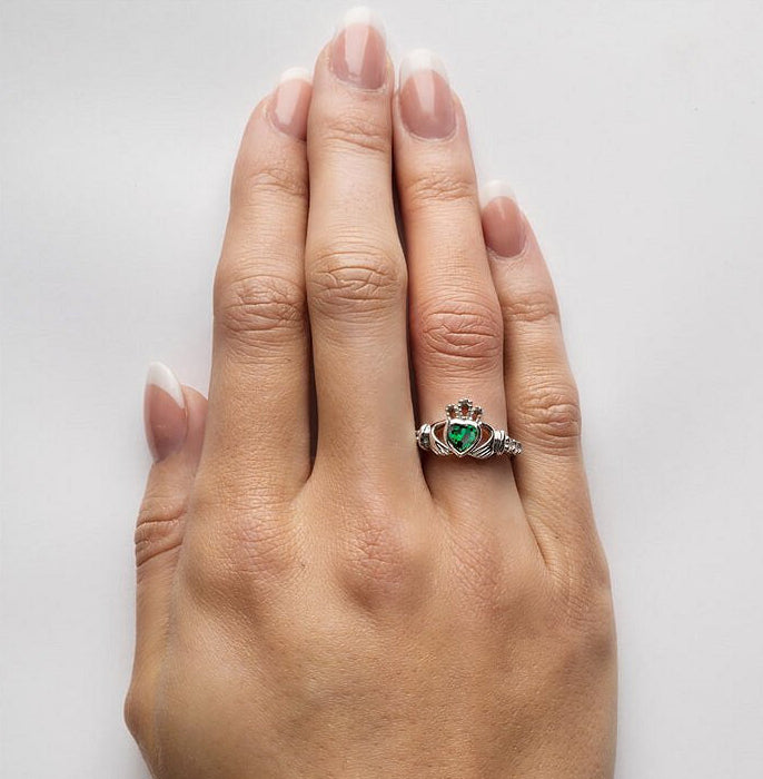 Silver claddagh ring with green cubic zirconia stone as heart, shown on a models hand.