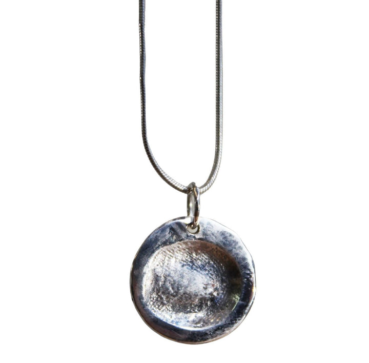 A Silver Clay Fingerprint pendant engraved with a fingerprint design hangs from a thin silver chain. This fingerprint pendant, with its slightly uneven, handmade appearance, offers a unique and personal touch. Produced by The Collective Dublin.