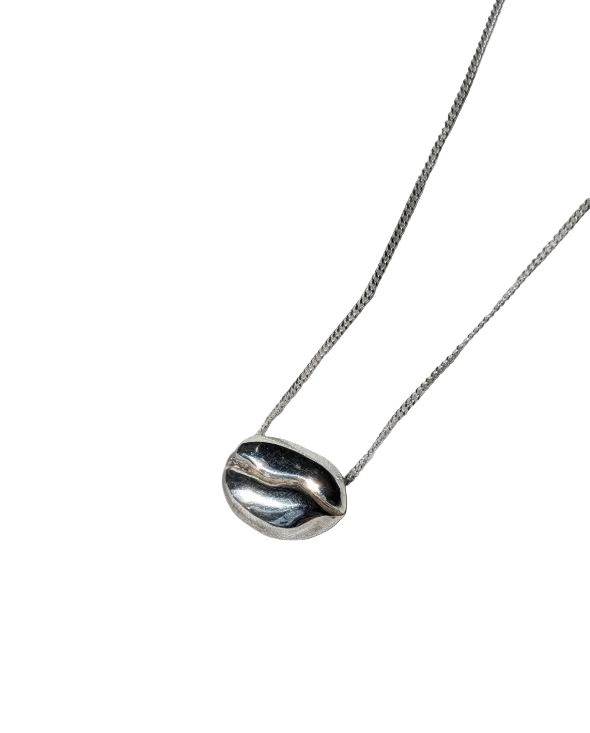 A polished silver pendant necklace in the style of a coffee bean on a silver chain against a white background 