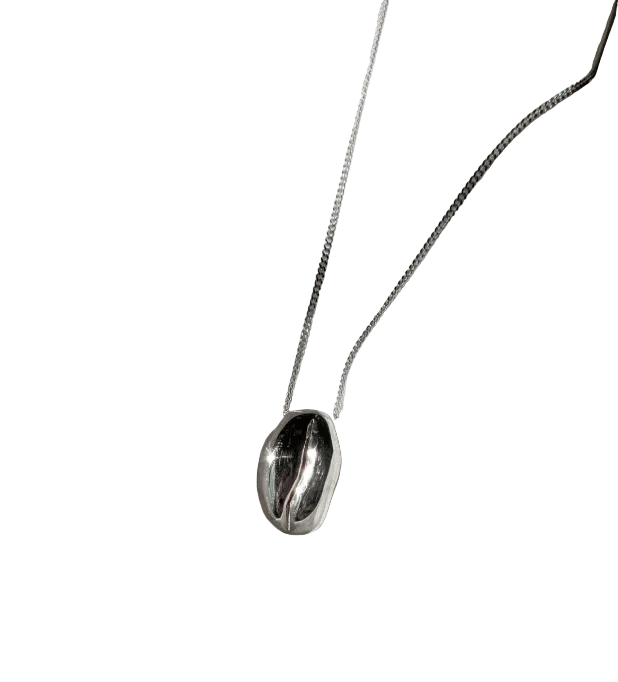 A polished silver pendant necklace in the style of a coffee bean on a silver chain in front of a white background.