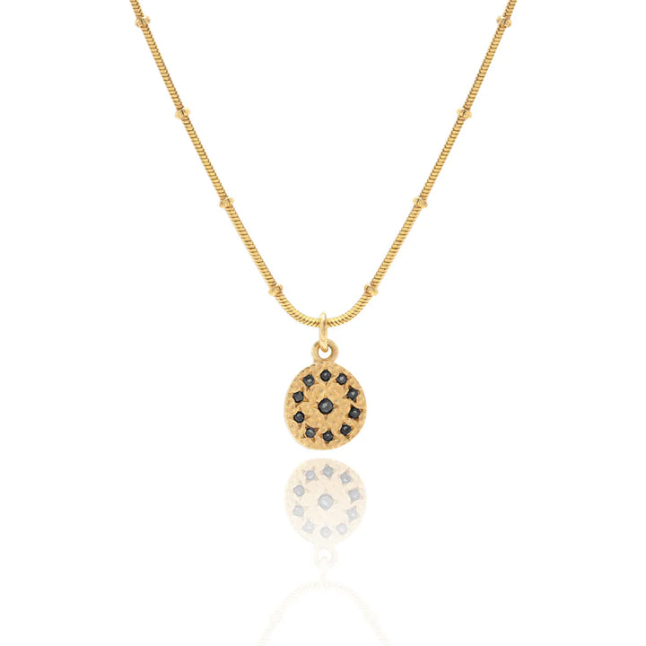 Gold necklace with a circular pendant featuring black stones on a white background