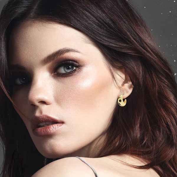 Close-up of a woman wearing gold earrings with a neutral background