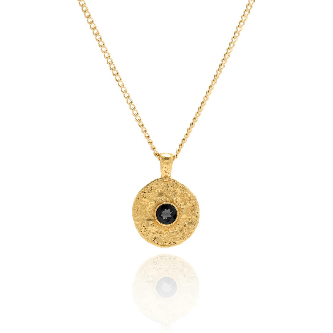 Gold necklace with a round pendant featuring a black gemstone on a white background
