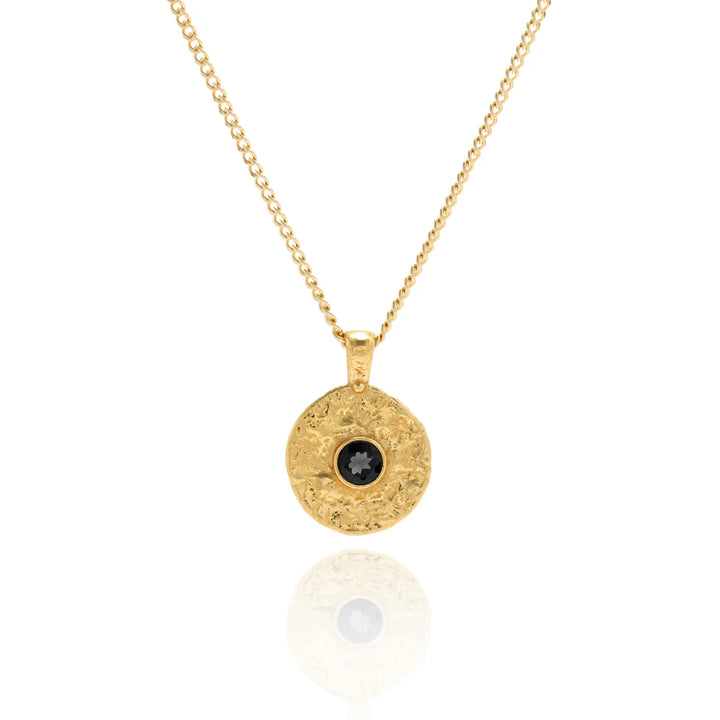 Gold necklace with a round pendant featuring a black gemstone on a white background