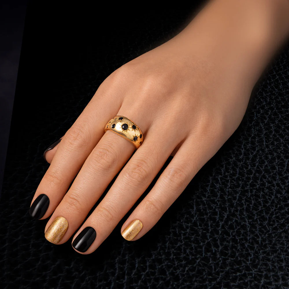 Hand wearing a gold ring with black and gold nail polish on a dark textured background