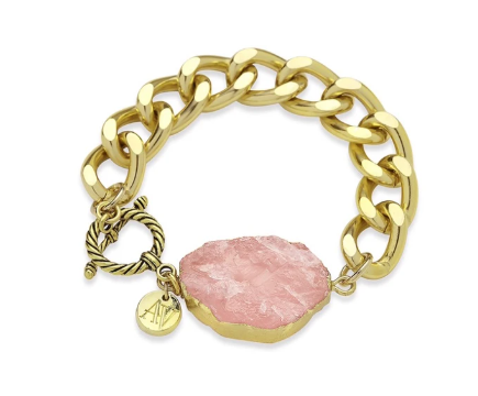 A stylish bracelet with chunky, gold-plated links, featuring a rough rose quartz stone charm and a small round gold tag engraved with "AHA." The clasp is a twisted gold circle and bar, all meticulously handmade in Dublin. Introducing the Cruise Chunky Bracelet by Aria V.