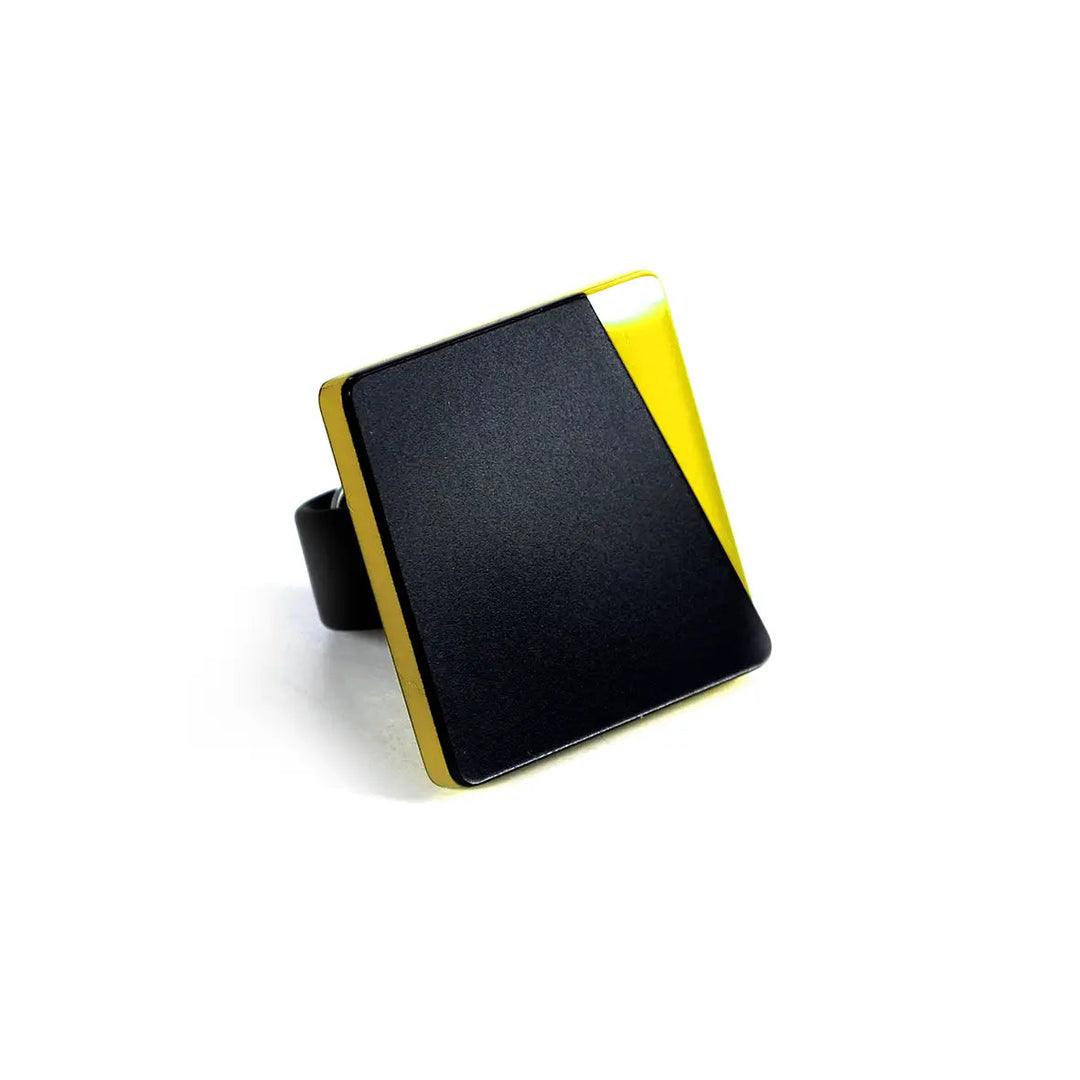 The Alex + Svet Saylor Ring made from high-quality acrylic glass features a black and yellow geometric design. The black band complements the modern, minimalist style of the rectangle, divided diagonally into two vibrant halves.