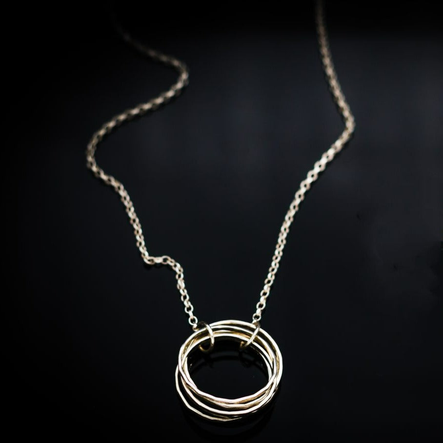 A delicate sterling silver chain necklace is centered with the Doorus Silver Pendant made of interwoven rings by Lynsey de Burca. The image has a sleek black background, highlighting the shine and simplicity of the jewelry design.