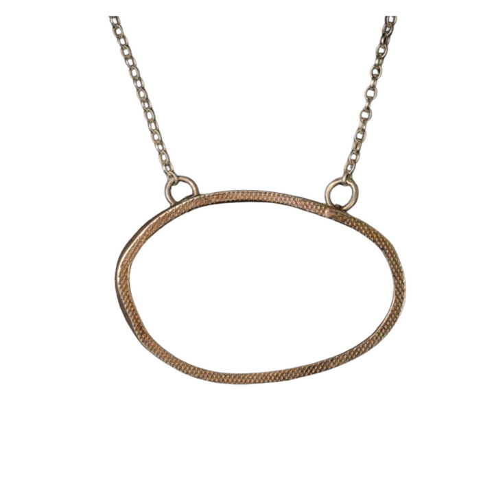 The Drift Pendant Gold by Lynsey de Burca is a gold chain necklace that showcases a large, asymmetrical oval-shaped, textured sterling silver pendant in the center. This pendant boasts an organic, freeform design and is connected to the chain by two loops. Handmade in Ireland, the chain features simple, interconnected links.