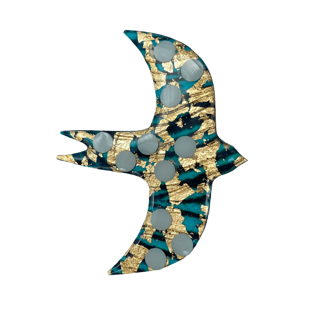 The Éan Bird Batik Textile Brooch by Rothlú showcases a bird motif on a blue background with gold leaf accents and circular white spots.