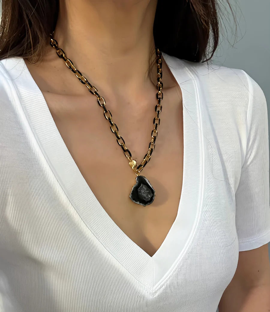 A woman in a white v-neck shirt wears the Eclipse Necklace by Aria V—a chunky gold and black enamel piece with a large, irregular handmade pendant crafted in Ireland.