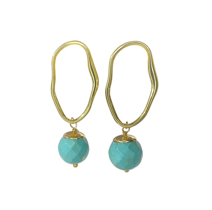 The Eddie Earrings by Aria V are gold plated, handmade in Ireland, and feature irregularly-shaped hoops with faceted turquoise beads dangling at the bottom, shown against a white background.