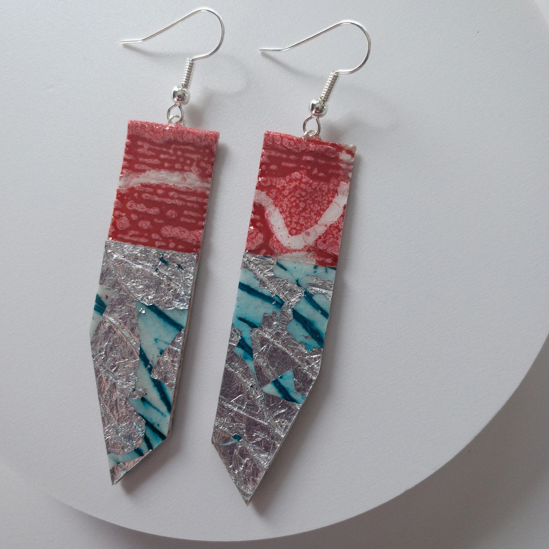 Long, geometric Edythe Batik Textile Earrings in Poppy/Silver/Aqua with a mix of patterns and textures: the top section is red with white speckles, the middle has a silver cracked texture, and the bottom features blue and white diagonal stripes. Each super-lightweight earring hangs from a simple sterling silver hook, making them truly one-of-a-kind. Brand Name: Rothlú