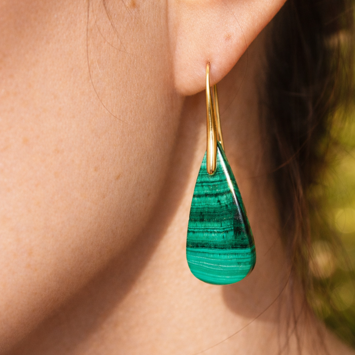 Close-up of a person’s ear wearing Kybalion Jewellery's Empress Earrings—a gold-plated statement piece featuring a teardrop green malachite gemstone with natural stripes. The skin is shown in soft focus.