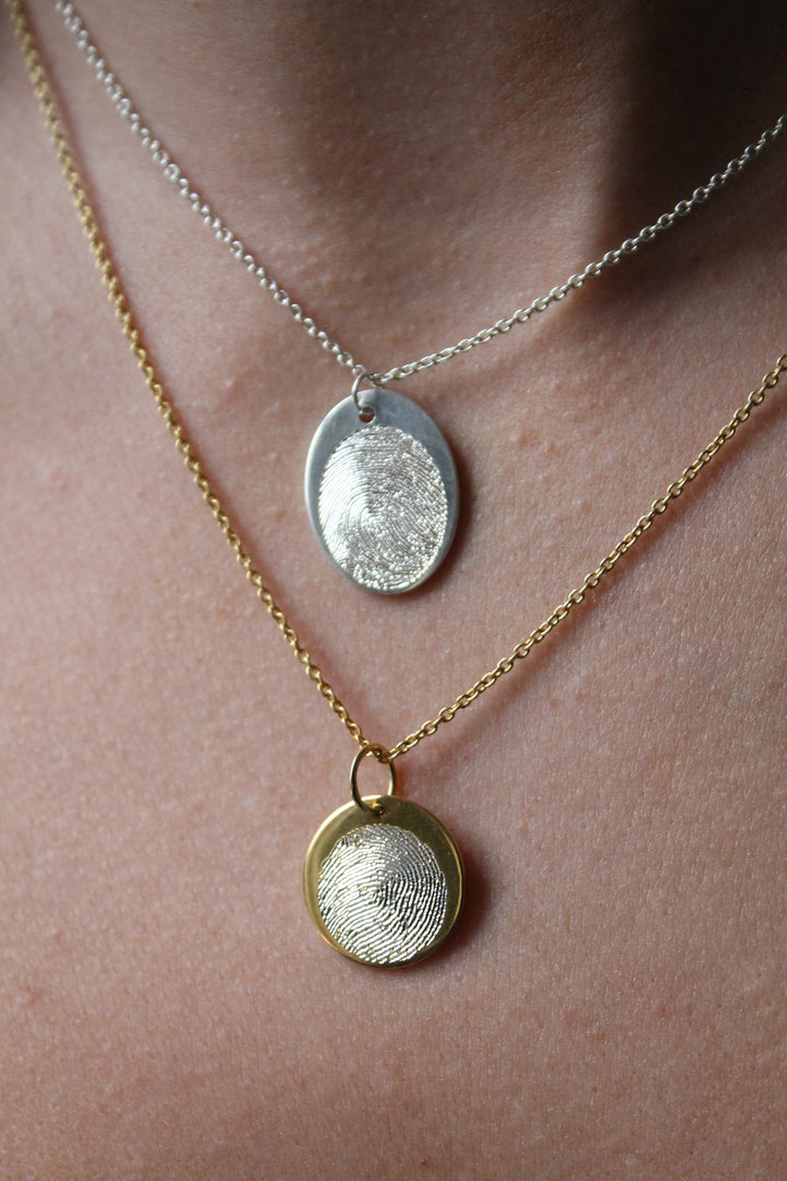 A person wearing two necklaces, both from Personalised Charms, features the Engraved Fingerprint Pendant on custom silver and gold chains.