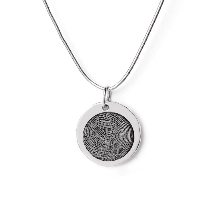 A silver necklace with a round pendant featuring a fingerprint engraving, perfect as a personalized gift. The Engraved Fingerprint Pendant by The Collective Dublin, customized to capture unique details, hangs from a thin, smooth chain against a plain white background.