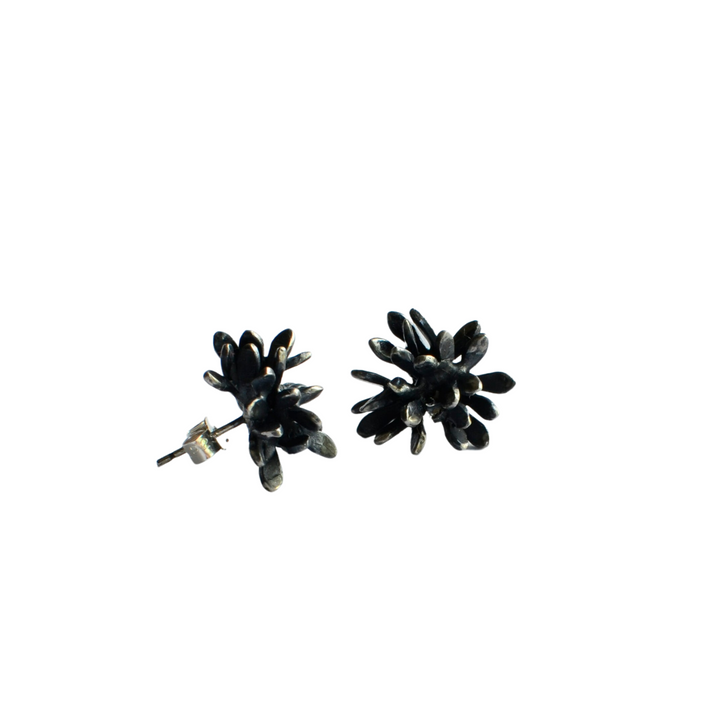 A pair of black flower-shaped stud earrings featuring numerous small petals and sterling silver backing clasps, the Folia Oxidised Silver Studs from Abbie Dixon are laid out against a plain white background, highlighting their intricate design and glossy finish in a captivating sculptural form.