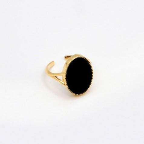 The Frida Ring by Nilai features a minimalist gold band adorned with an oval-shaped natural stone in black, set elegantly at its center. The ring's smooth, polished finish stands out against a plain white background.