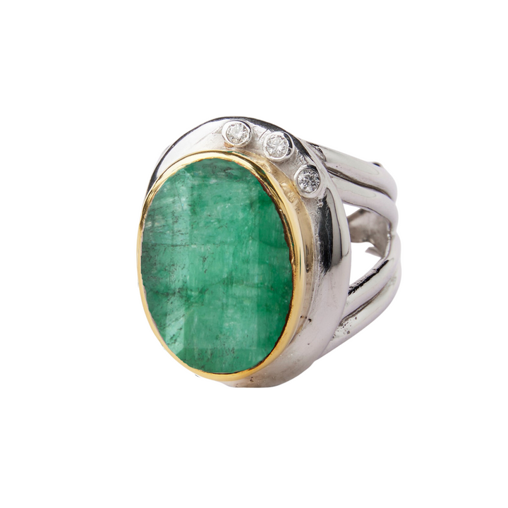 A silver statement cocktail ring featuring a large, oval-shaped green gemstone, likely an emerald, set in a gold bezel. The ring boasts a split shank design and includes three small round diamonds embedded into the bezel above the emerald. A true showcase of colourful gemstones. This exquisite piece is the Eyetelia Ring in various gemstones by Gallardo & Blaine Designs.