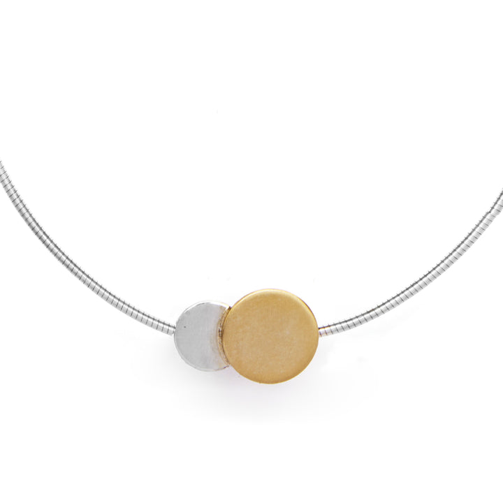 The Gallardo & Blaine Designs Archeol Necklace in Sterling Silver & Gold Vermeil features a minimalist thin metallic chain with two overlapping circular pendants. One pendant is crafted from gold vermeil, and the other from sterling silver. The design is simple and elegant, exuding a modern and timeless aesthetic.