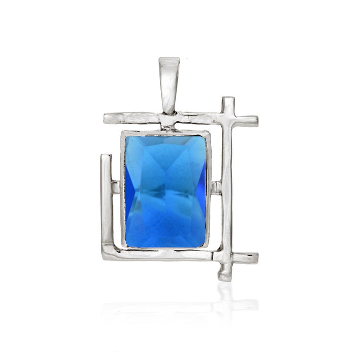 The Art Deco Pendant in various gemstones by Gallardo & Blaine Designs is a rectangular sterling silver pendant with an abstract design, featuring a prominent blue rectangular gem at the center. The silver frame has geometric, angled lines, reminiscent of an Art Deco style, giving it a modern and artistic look.