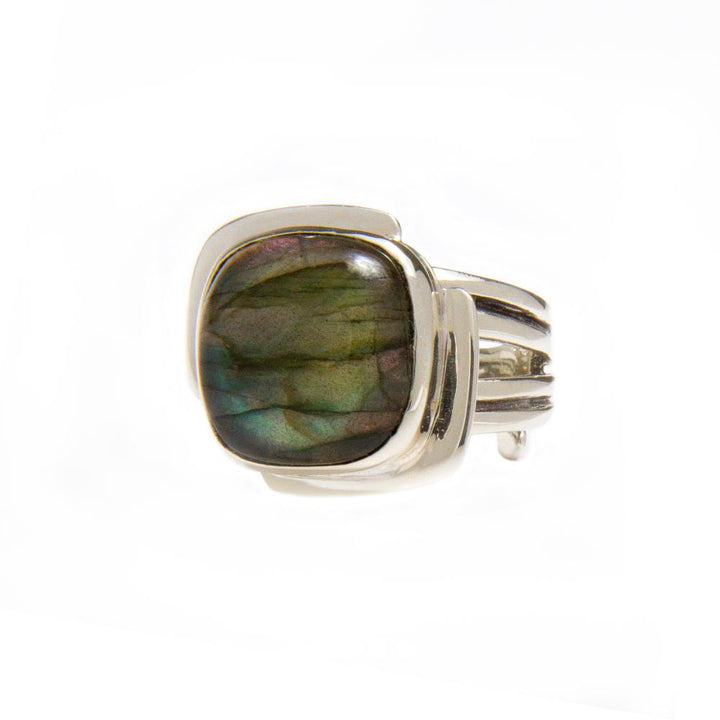 A Gallardo & Blaine Designs Art Deco Ring in Silver Gold & various gemstones featuring a large, polished, multicolored rectangular gemstone with shades of green, blue, and purple. The stone is set in a modern, wide band design with three split shanks on each side leading to the stone. The background is plain white.