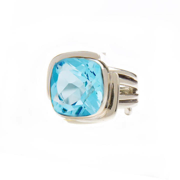 A Gallardo & Blaine Designs Art Deco Ring in Silver Gold & various gemstones featuring a large, square-cut blue gemstone in the center. The faceted gemstone adds to its sparkle. With a modern design and multiple thin bands converging at the back, this Art Deco ring is set against a white background, highlighting its elegance.