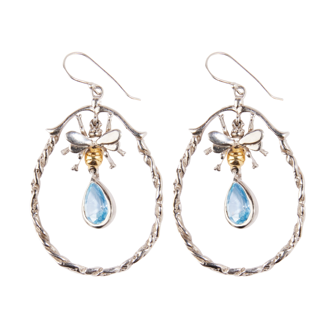 A pair of elegant Wildlife Large Bee Hoop Drops in various gemstones featuring intricate silver bees with gold-toned bodies. Each bee holds a teardrop-shaped blue gemstone drop, suspended within twisted sterling silver hoops. The earrings have hook-style clasps for easy wearing by Gallardo & Blaine Designs.