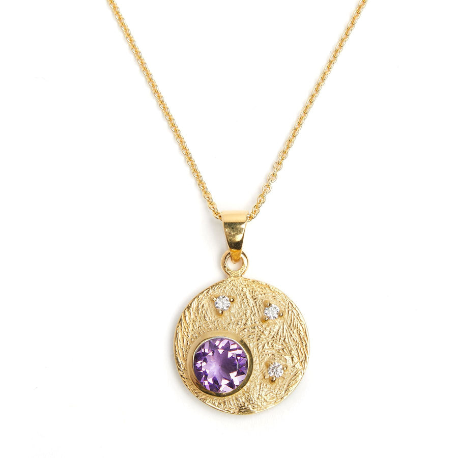 A gold Celeste Necklace in Gold & various gemstones by Gallardo & Blaine Designs featuring a pendant with a textured round disk. The gemstone pendant has a large central purple gemstone and three smaller cubic zirconia stones inset around it. The chain is delicate and finely linked.