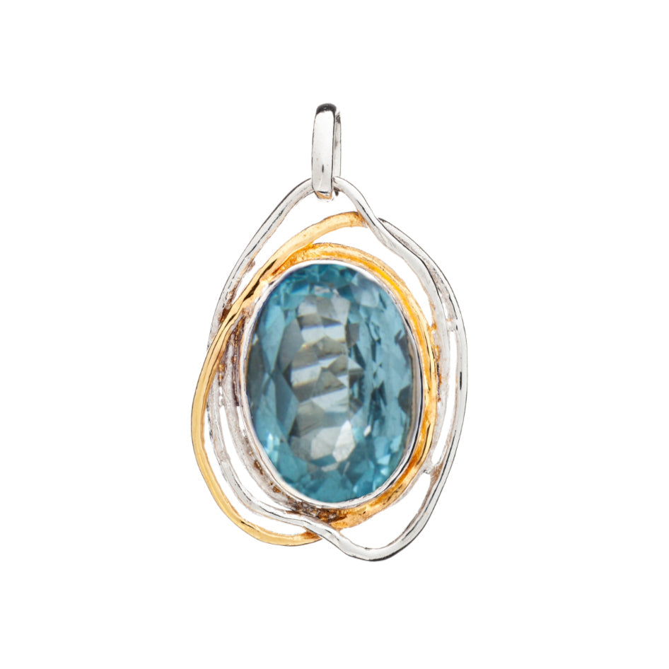 The statement gemstone pendant, known as the Cosmos Pendant Large in various gemstones by Gallardo & Blaine Designs, features an oval blue gemstone with a faceted surface set in a mixed metal frame. The frame boasts intertwining silver and gold-toned loops, creating an elegant yet artistic design reminiscent of medieval times. A small loop at the top allows for easy attachment to a chain.