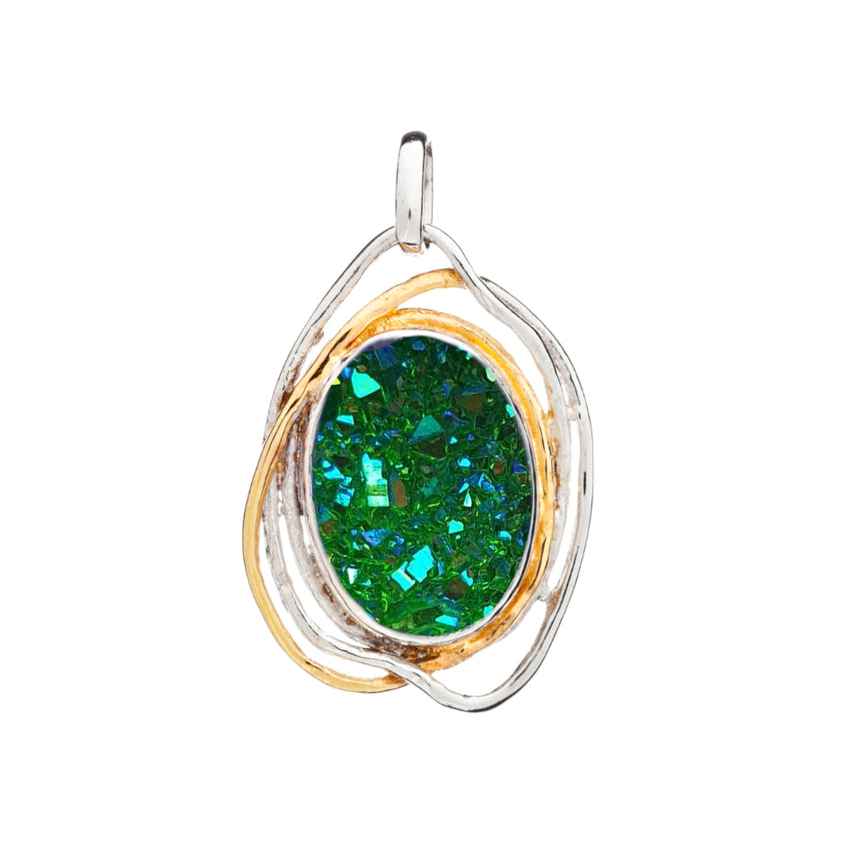 A Cosmos Pendant Large in various gemstones by Gallardo & Blaine Designs featuring a vibrant, emerald-green, oval-shaped gemstone with a druzy texture. The gem is set in a silver and gold intertwined metal frame, creating an elegant and artistic design reminiscent of medieval craftsmanship. The pendant has a small loop at the top for attachment to a chain.