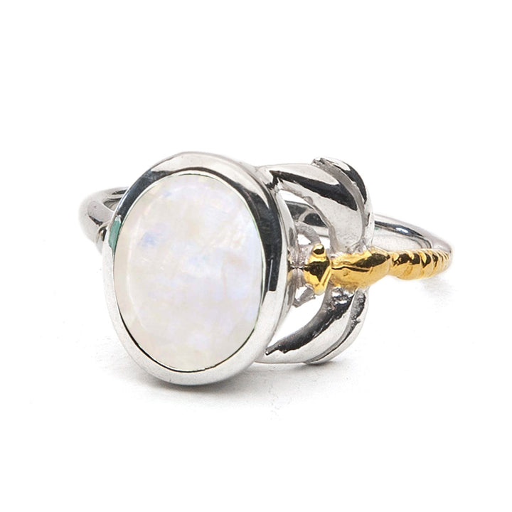 A close-up of the Daydream Ring in various gemstones by Gallardo & Blaine Designs featuring a polished oval gemstone set in a silver band with intricate gold accents. This timeless piece has a pearlescent sheen, reflecting light in various colors, and the delicate and dainty band includes decorative silver and gold elements that add to its elegance.