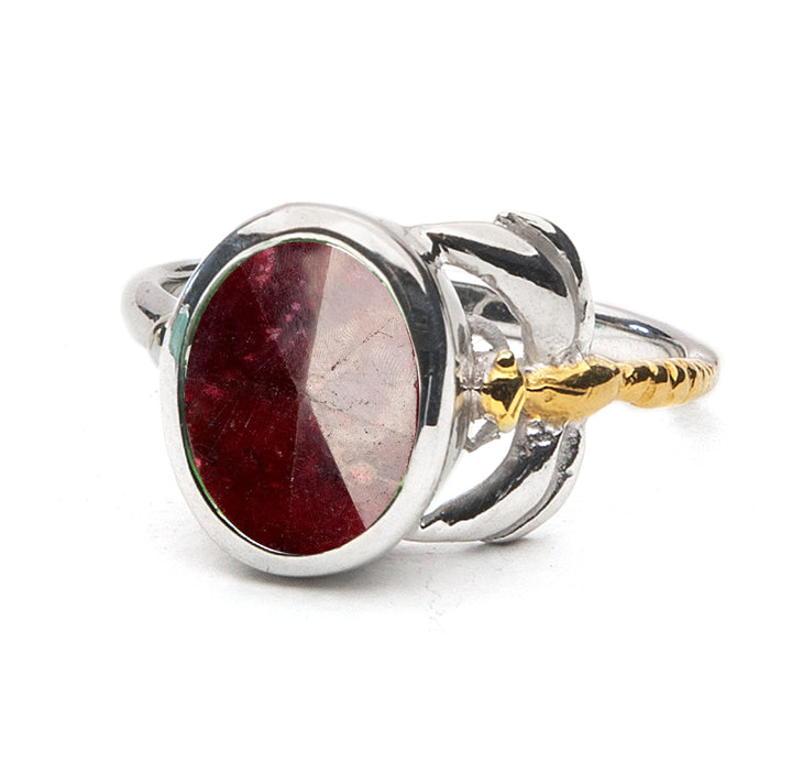 A silver ring featuring a large, oval-shaped red gemstone set in the center. The band has intricate detailing with a mix of silver and gold tones, creating a unique, elegant design. This timeless piece boasts a faceted surface that catches the light beautifully. The Gallardo & Blaine Designs Daydream Ring in various gemstones is perfect for adding a touch of sophistication to any outfit.