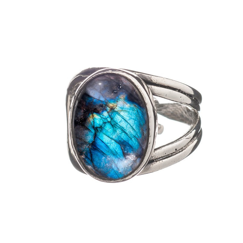 A Gallardo & Blaine Designs Dewberry Ring in various gemstones, featuring an oval-shaped, polished labradorite stone. The stone showcases vibrant shades of blue, green, and a bit of metallic sheen. The adjustable ring band has a split design, adding an elegant touch to this chunky statement piece. White background.