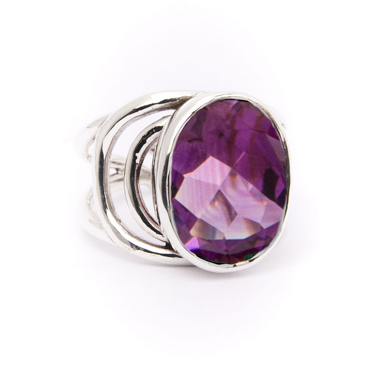 The Dewberry Ring by Gallardo & Blaine Designs features a bold, oval-cut purple gemstone with a faceted finish, set in a sleek open sterling silver band, shown on a white background.