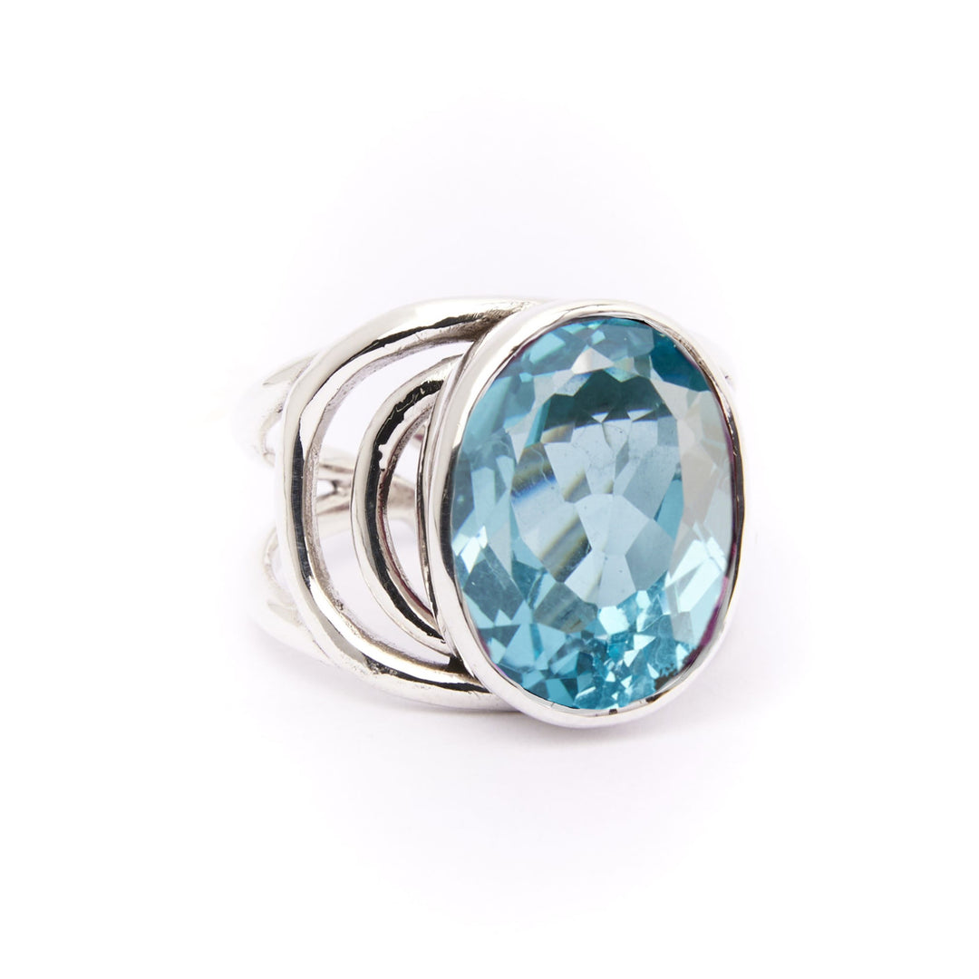 The Gallardo & Blaine Designs Dewberry Ring features an open sterling silver band and a large, oval blue gemstone—a bold, modern statement piece in striking contrast against any background.