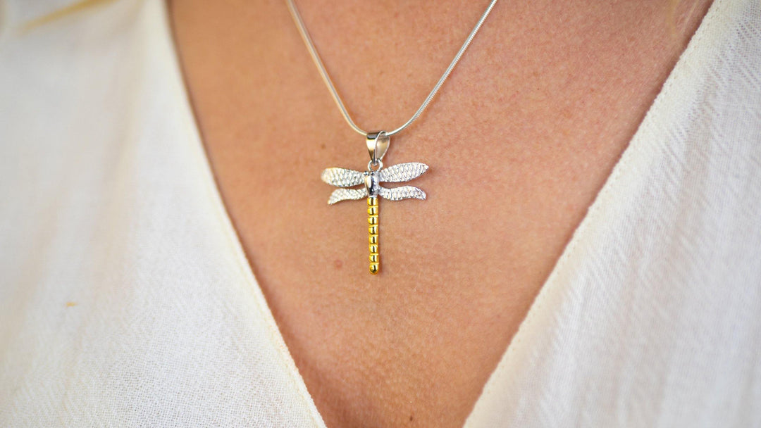 A Wildlife Pendant - Large Dragonfly With Chain from Gallardo & Blaine Designs hangs on a delicate silver snake chain around a person's neck. The person is wearing a light-colored, textured top, showcasing the exquisite piece from the Wildlife Collection.