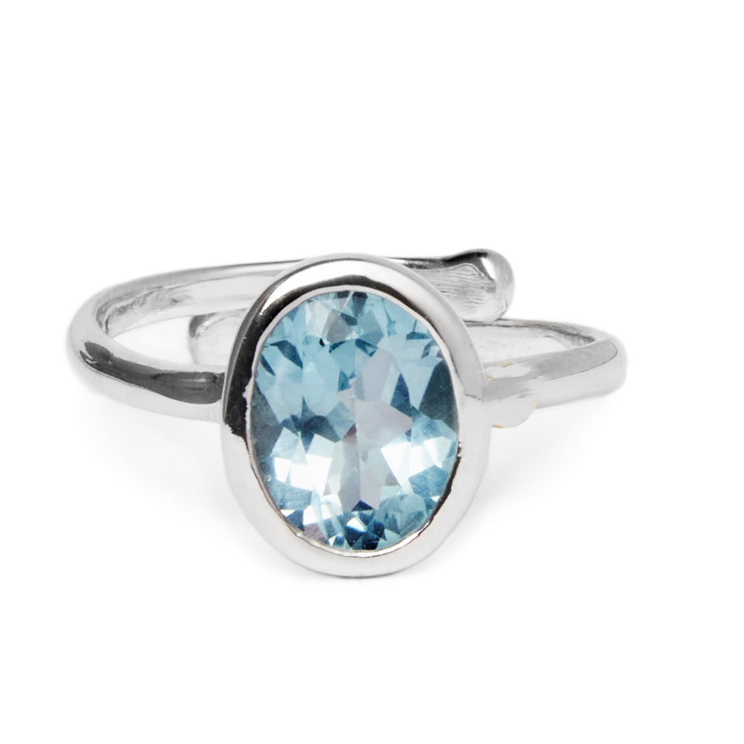 The Dream Ring in various gemstones by Gallardo & Blaine Designs is a sterling silver, adjustable ring featuring an oval-shaped blue gemstone set in a simple band. The gemstone has facets that catch the light, creating subtle highlights and reflections. The minimalist design is complemented by the smooth, polished finish of the band.