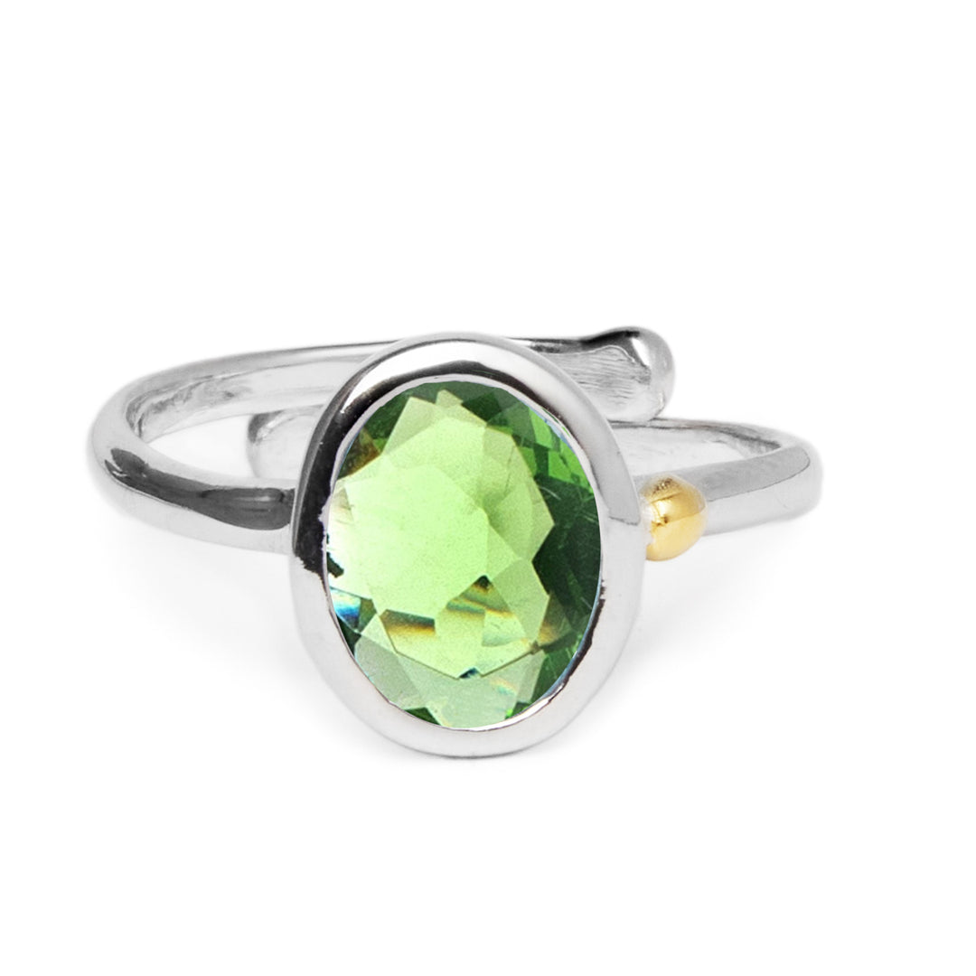 The Adjustable Dream Ring by Gallardo & Blaine Designs features an oval faceted green gemstone at its center. Crafted from sterling silver, it showcases a sleek, minimalist band with a small gold accent near the gem for an effortlessly stylish look.