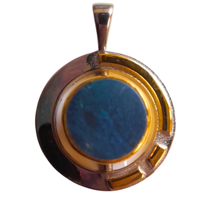 The Elodie Pendant in silver gold & various gemstones by Gallardo & Blaine Designs features a round, blue gemstone set in a circular, silver-colored metal frame. The Art Deco design includes a gold-colored band encircling the gemstone and extending into the geometric cutout details of the shiny frame.